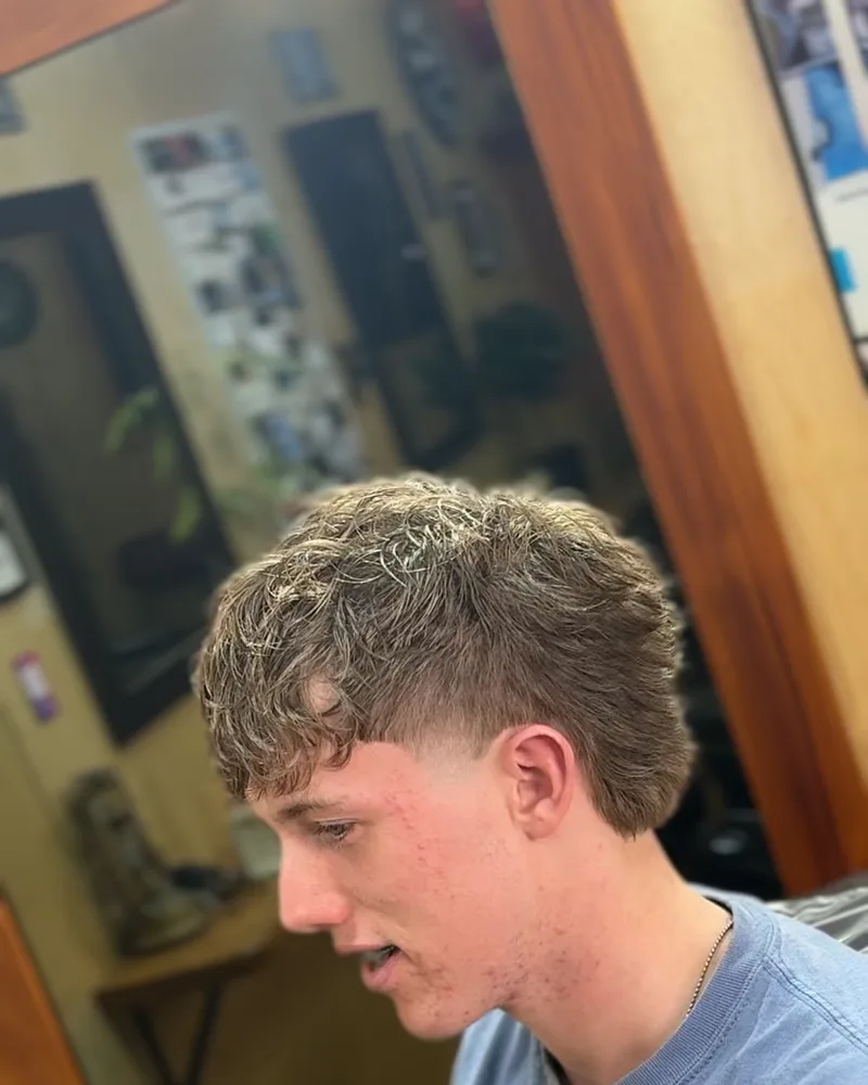 A textured curly fringe cut with a low taper at the sides, seen in the mirror